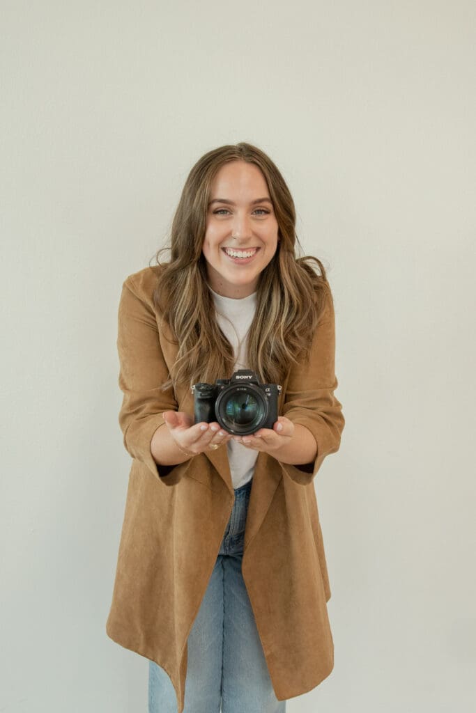 Brooke, a Texas elopement photographer, smiles at the camera with her camera placed delicately in her palms.