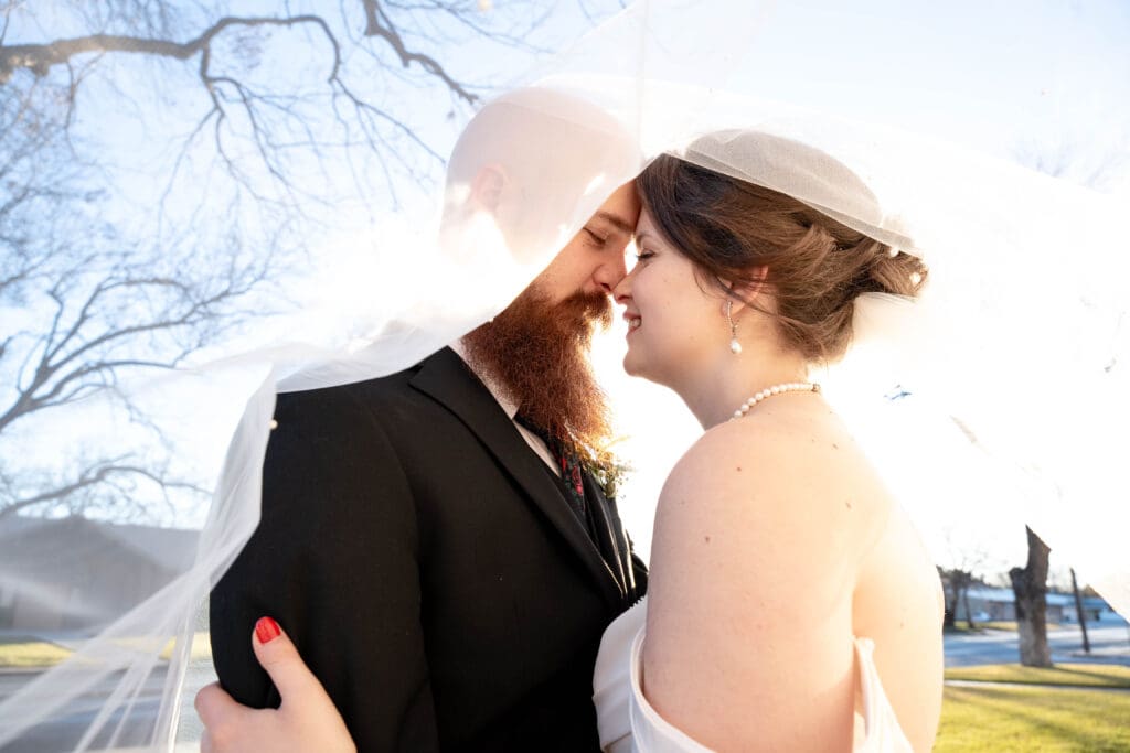 Bride and groom cuddle up nose to nose under a white veil - Winter when to elope in texas