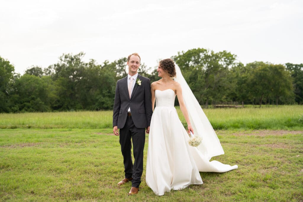 bride and groom walk towards the camera in a green field - Spring where to elope in texas