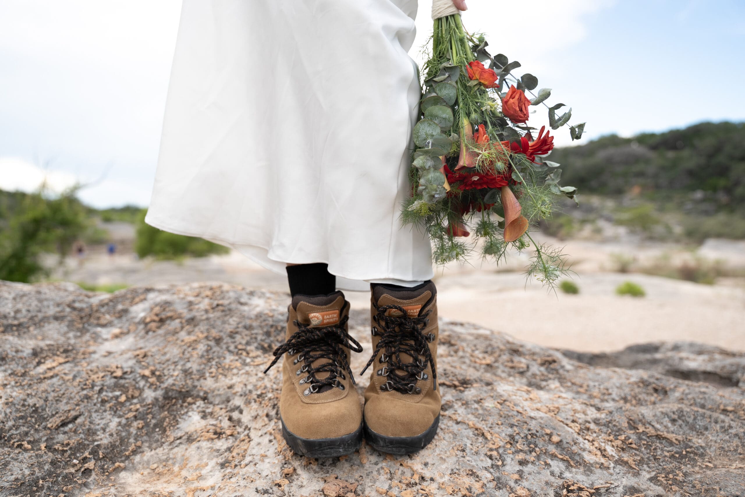 Bride in her hiking boots and wedding dress holding a boho bouquet