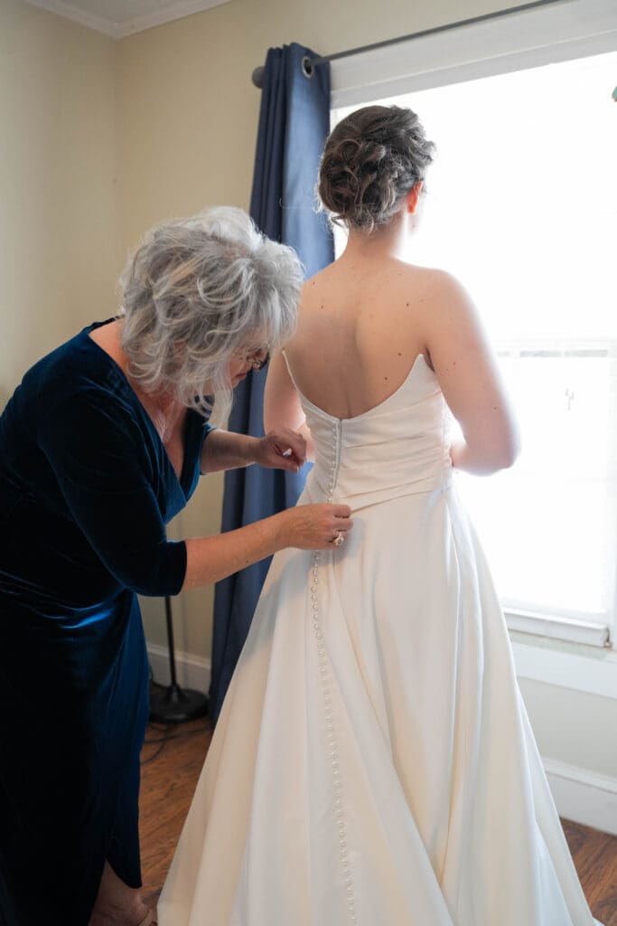 Mother of bride buttoning bride's dress