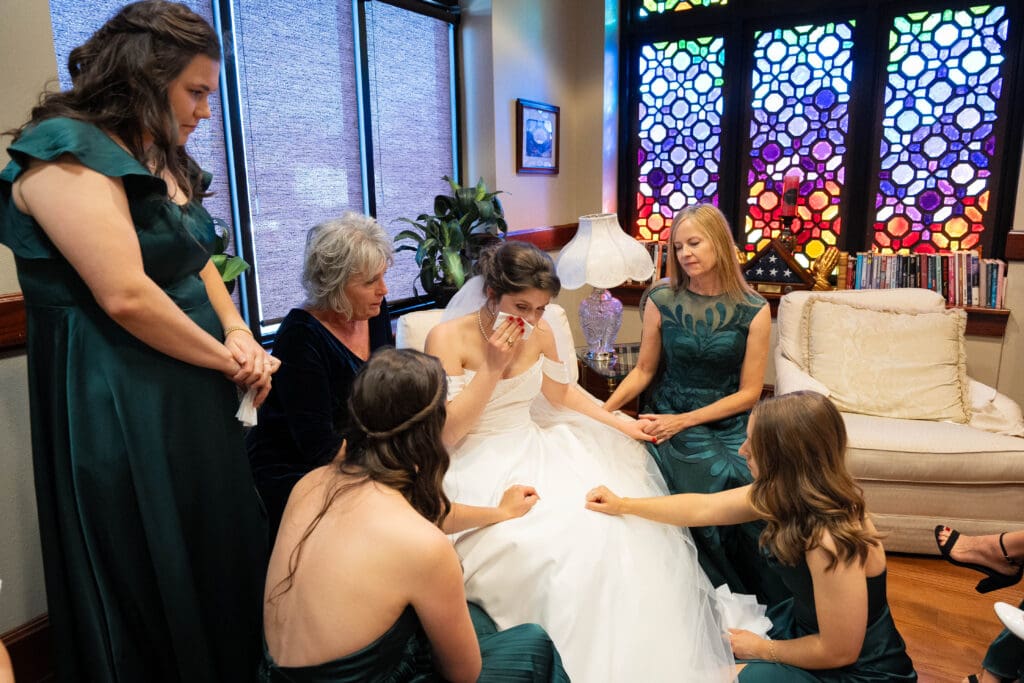 Bridesmaids pray over bride in colorful church room