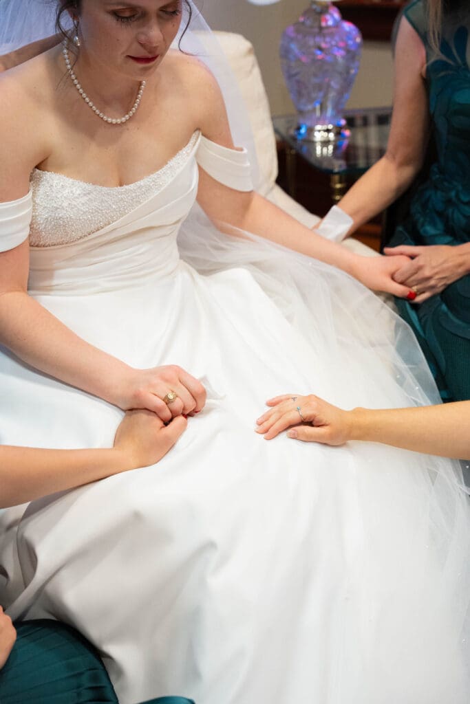 Close up on bride as bridesmaids pray over her